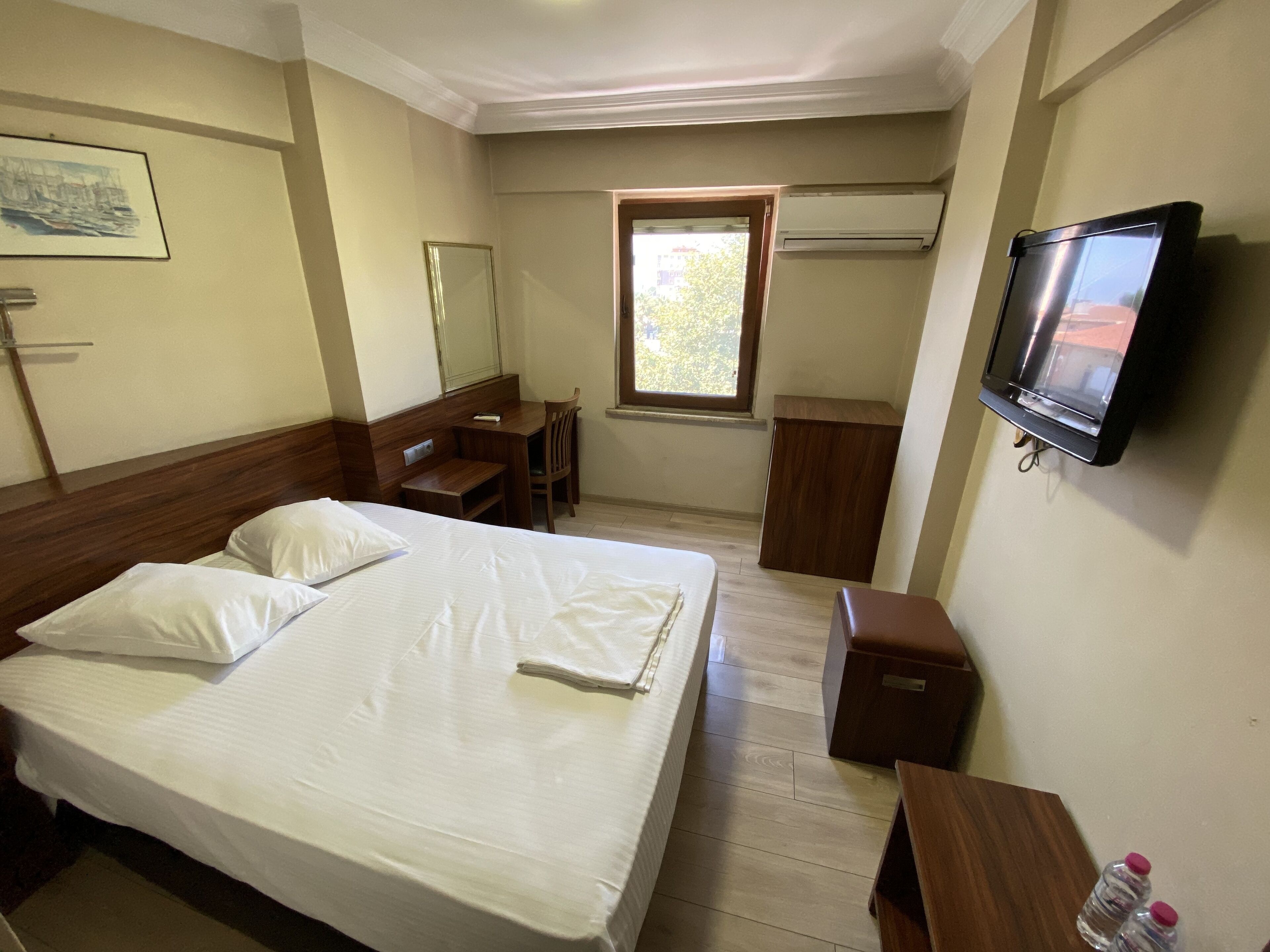 A hotel room with a bed, a desk, a chair, a TV, and a window.