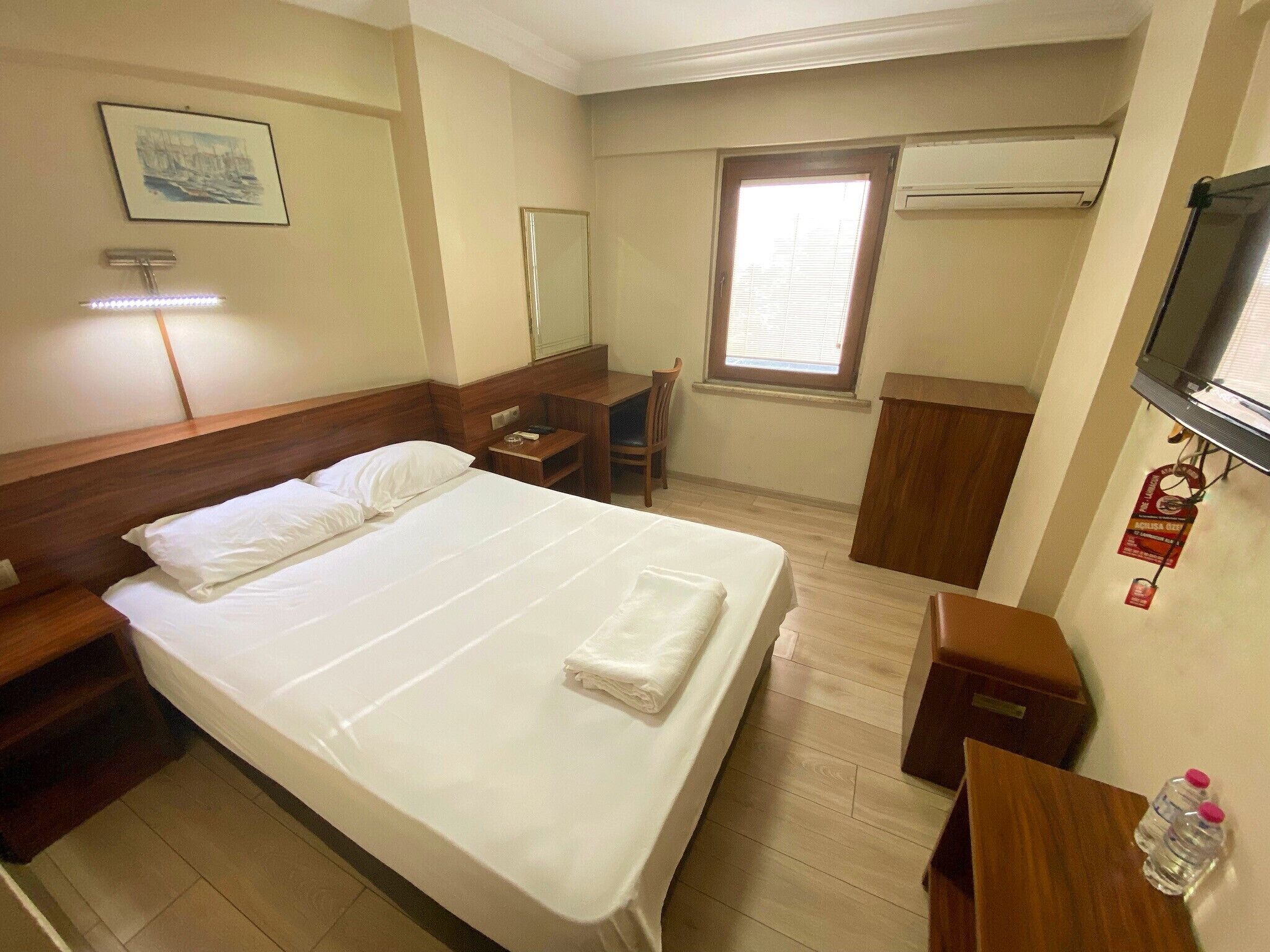 A hotel room with a large bed, a desk, a chair, a TV, and a window.