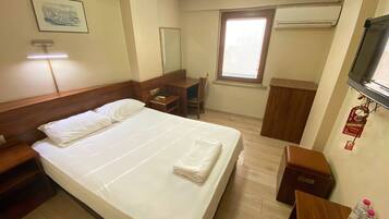 A hotel room with a large bed, a desk, a chair, a TV, and a window.