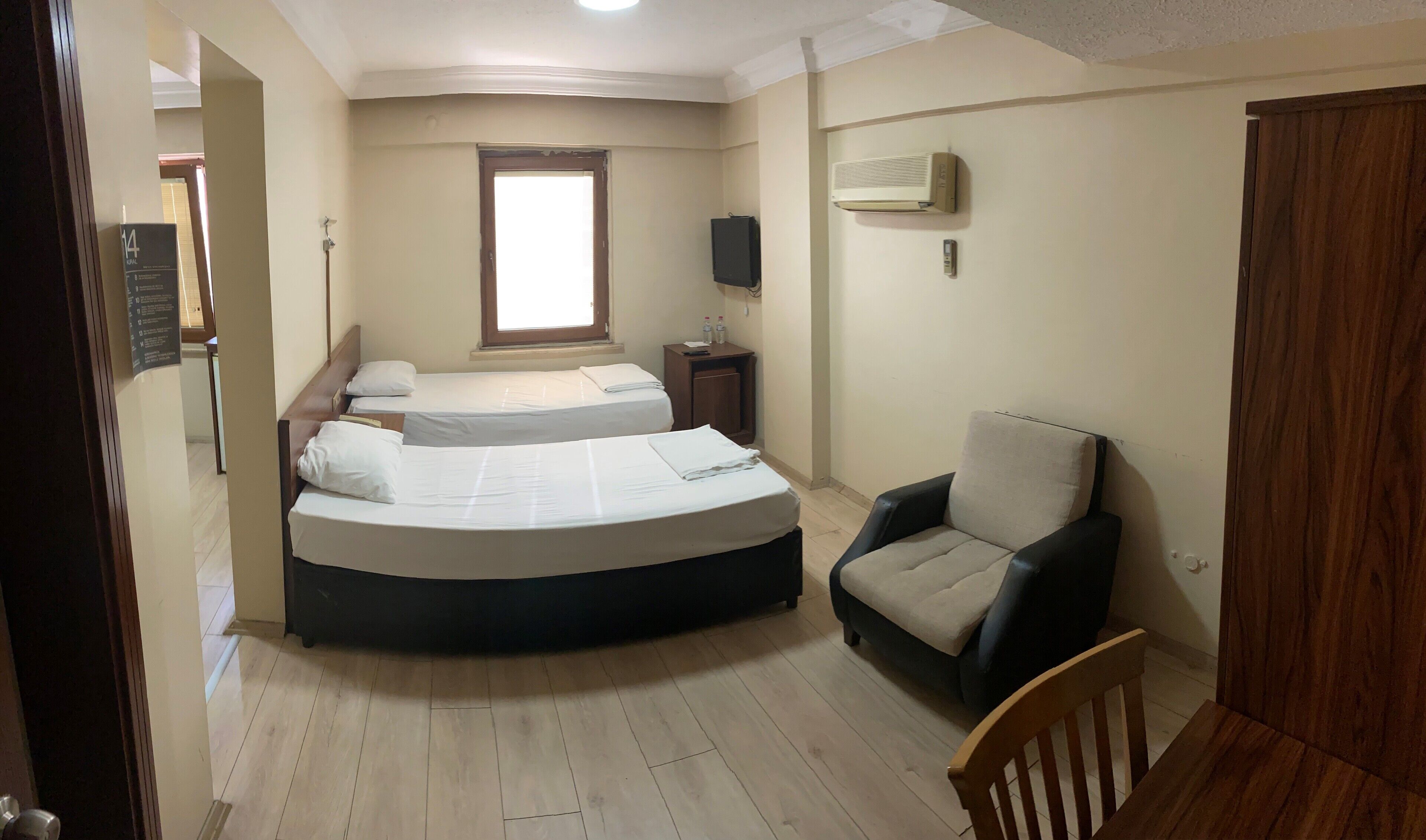 A bedroom with two beds, a chair, a TV, and an air conditioner.
