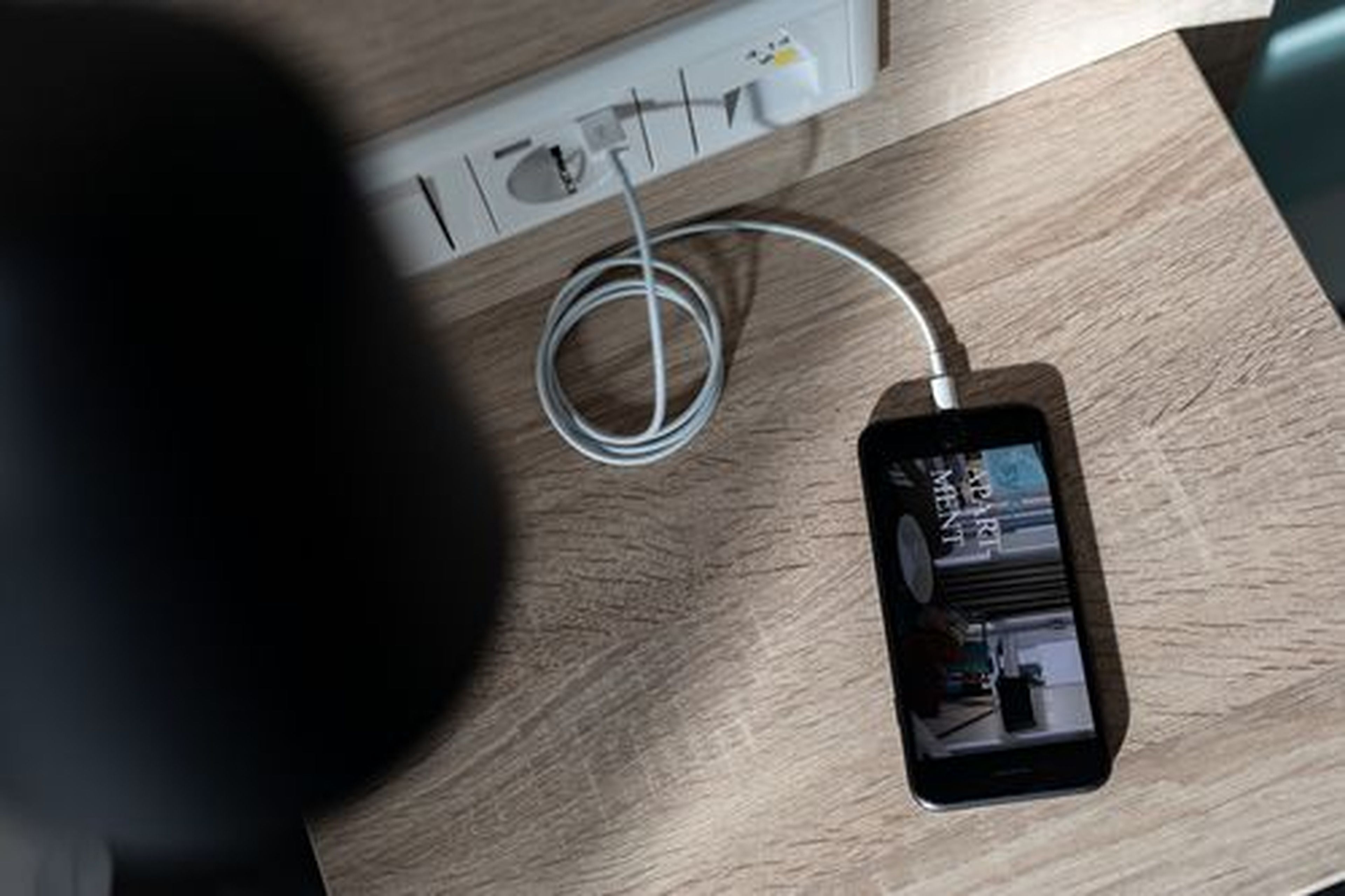 A smartphone connected to a power source on a wooden surface.