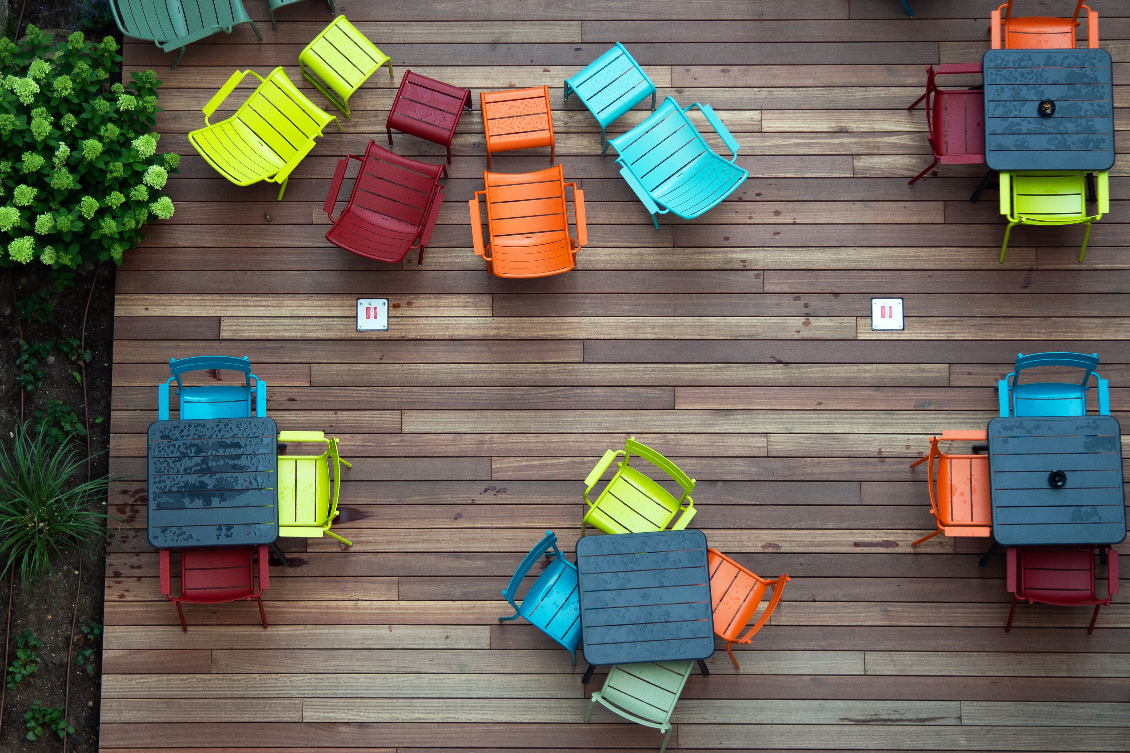 A top-down view of a wooden deck with multiple colorful chairs and tables arranged in a circular pattern.