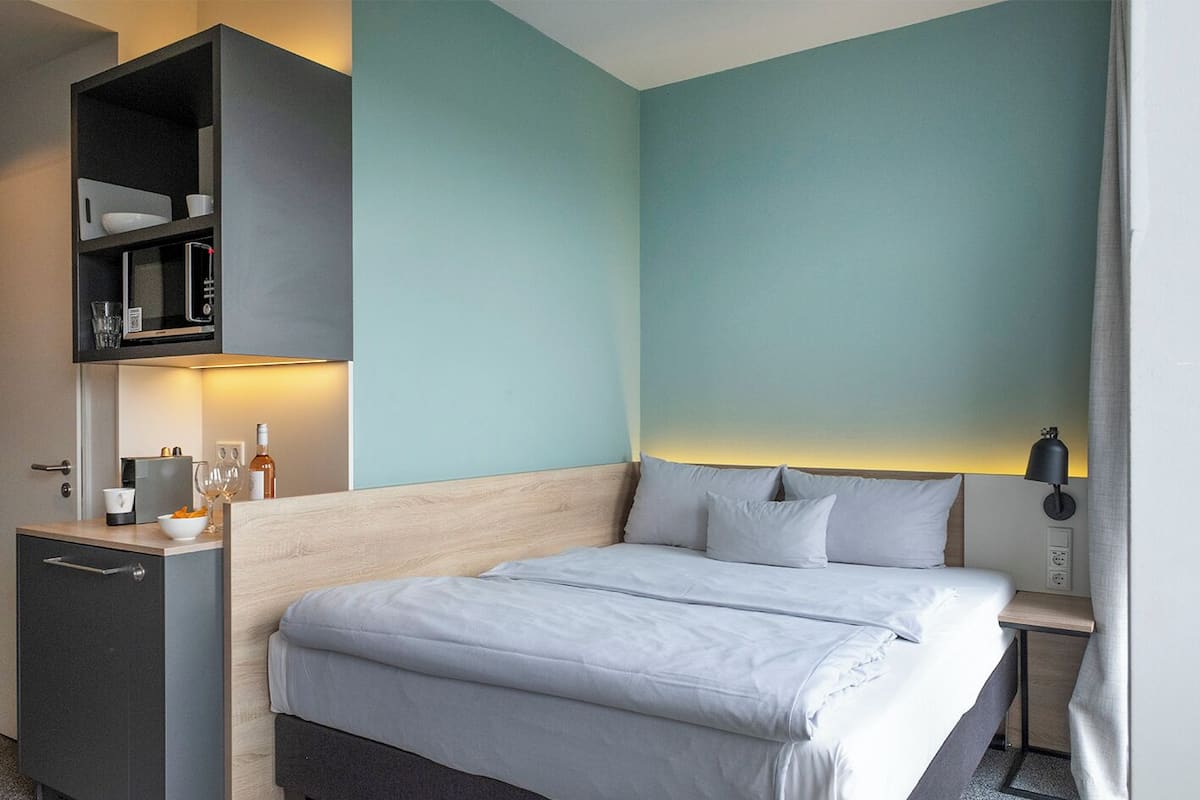 Ein Hotelzimmer mit Bett, Nachttisch und einer eingebauten Ablage mit Küchenutensilien.