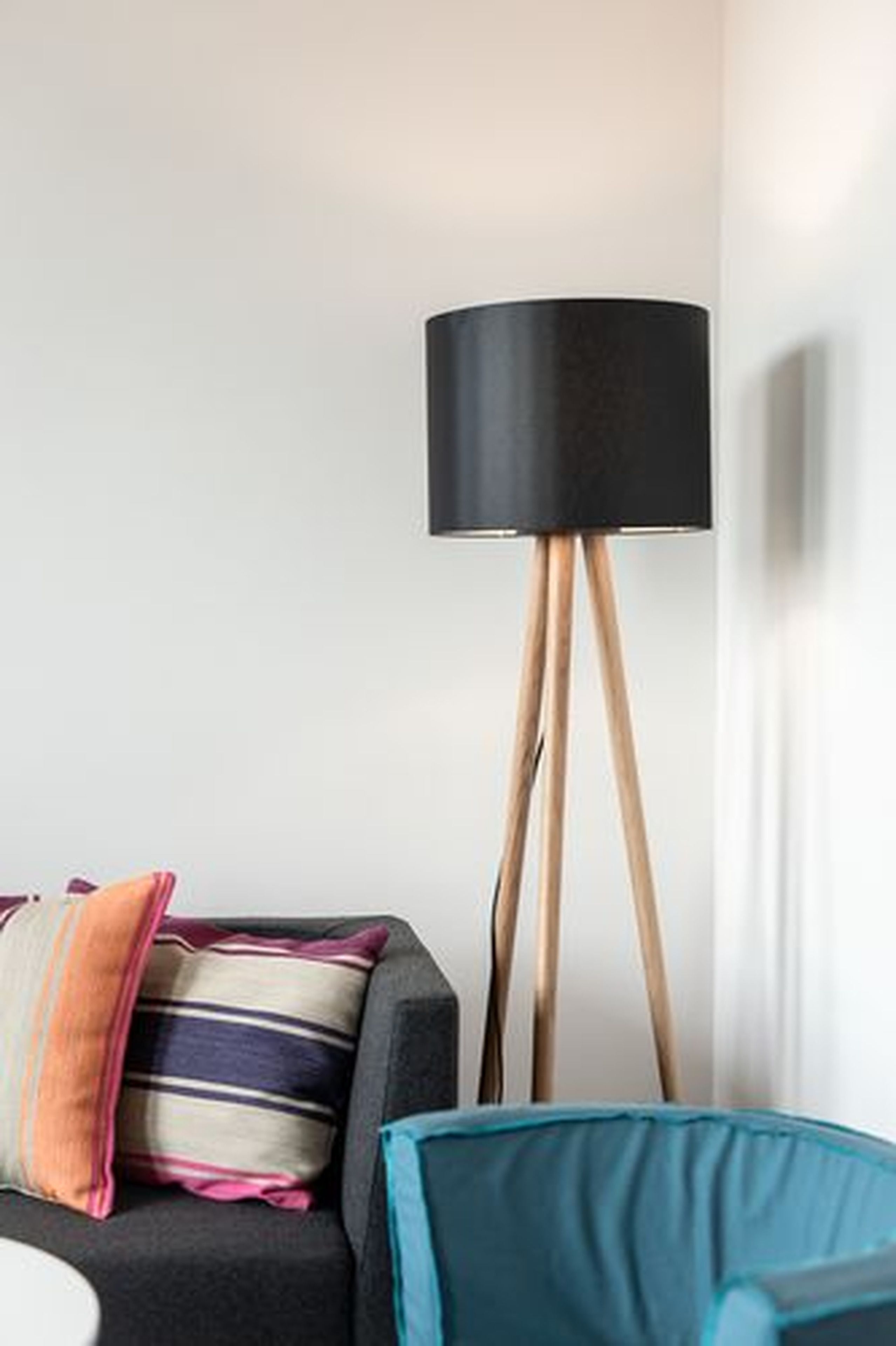 A modern living room with a black sofa, colorful cushions, a blue armchair, and a floor lamp with a black shade.