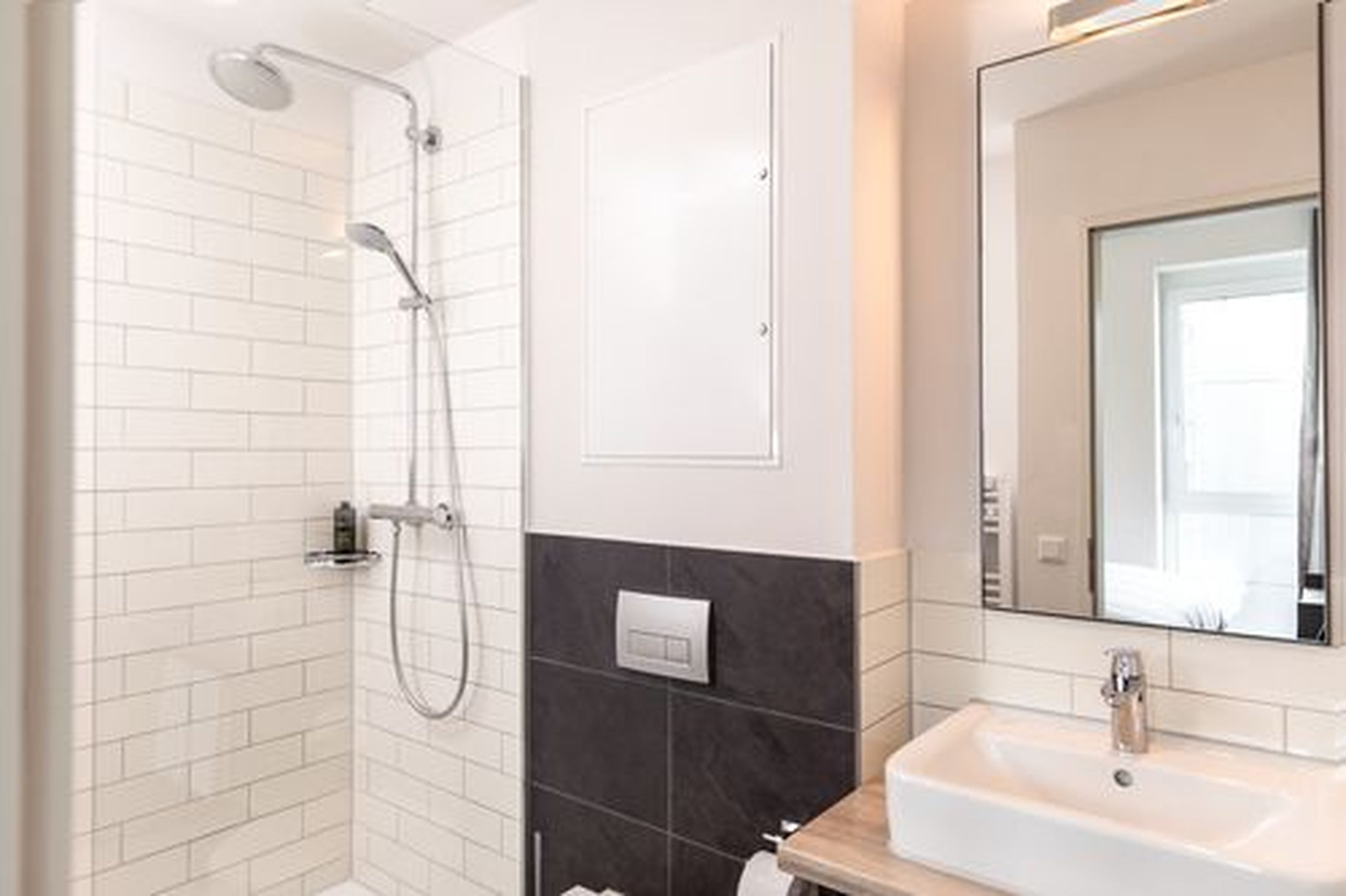 A modern bathroom with white and dark tiles, a shower, a sink, and a mirror.