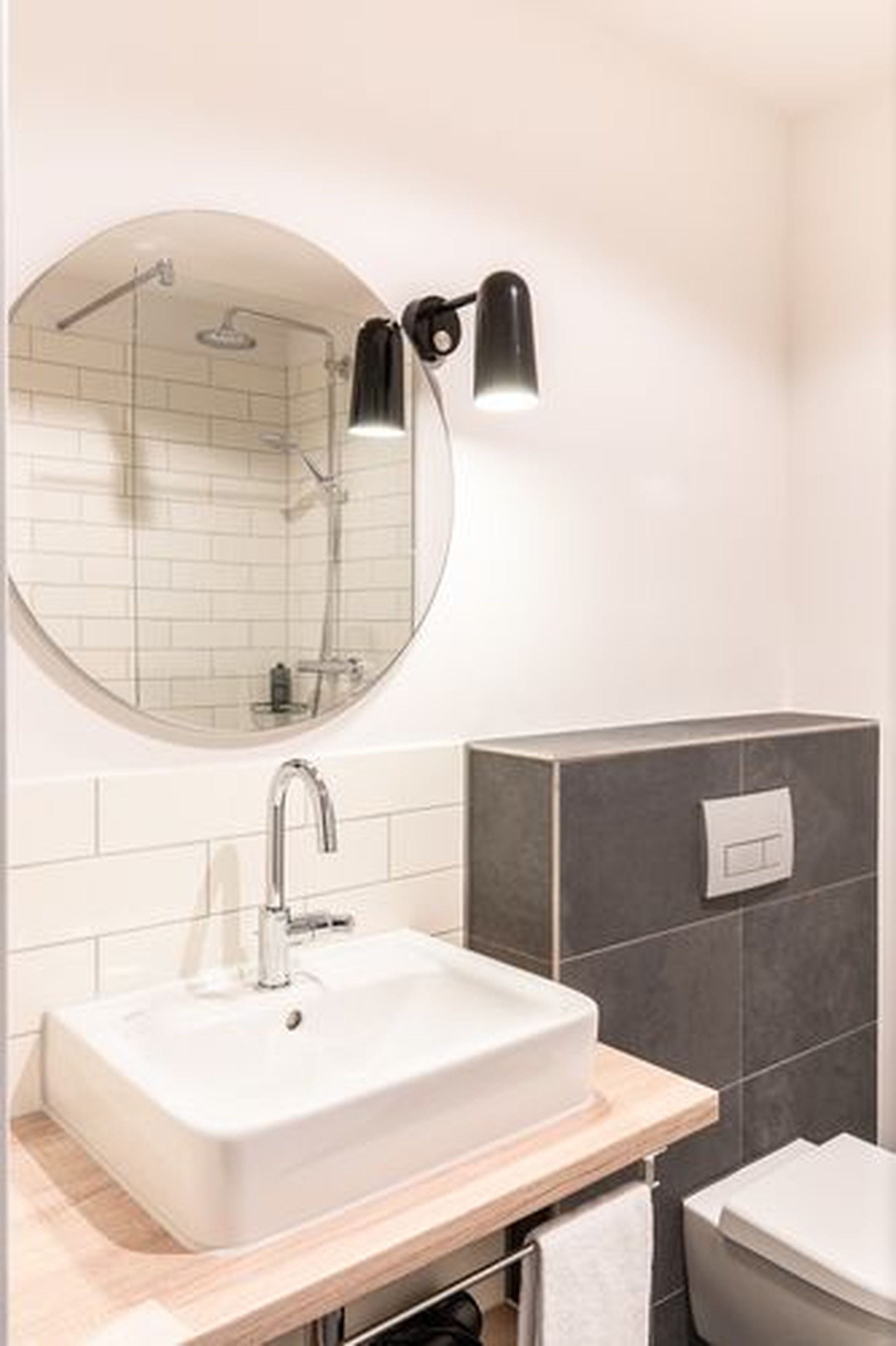 A modern bathroom with a round mirror, a rectangular sink, a shower, and a toilet.