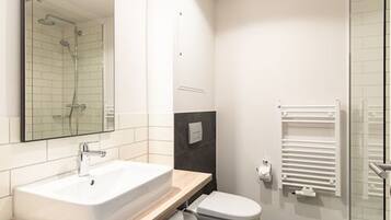 A modern bathroom with a large mirror, a bathtub, a toilet, and a glass shower enclosure.