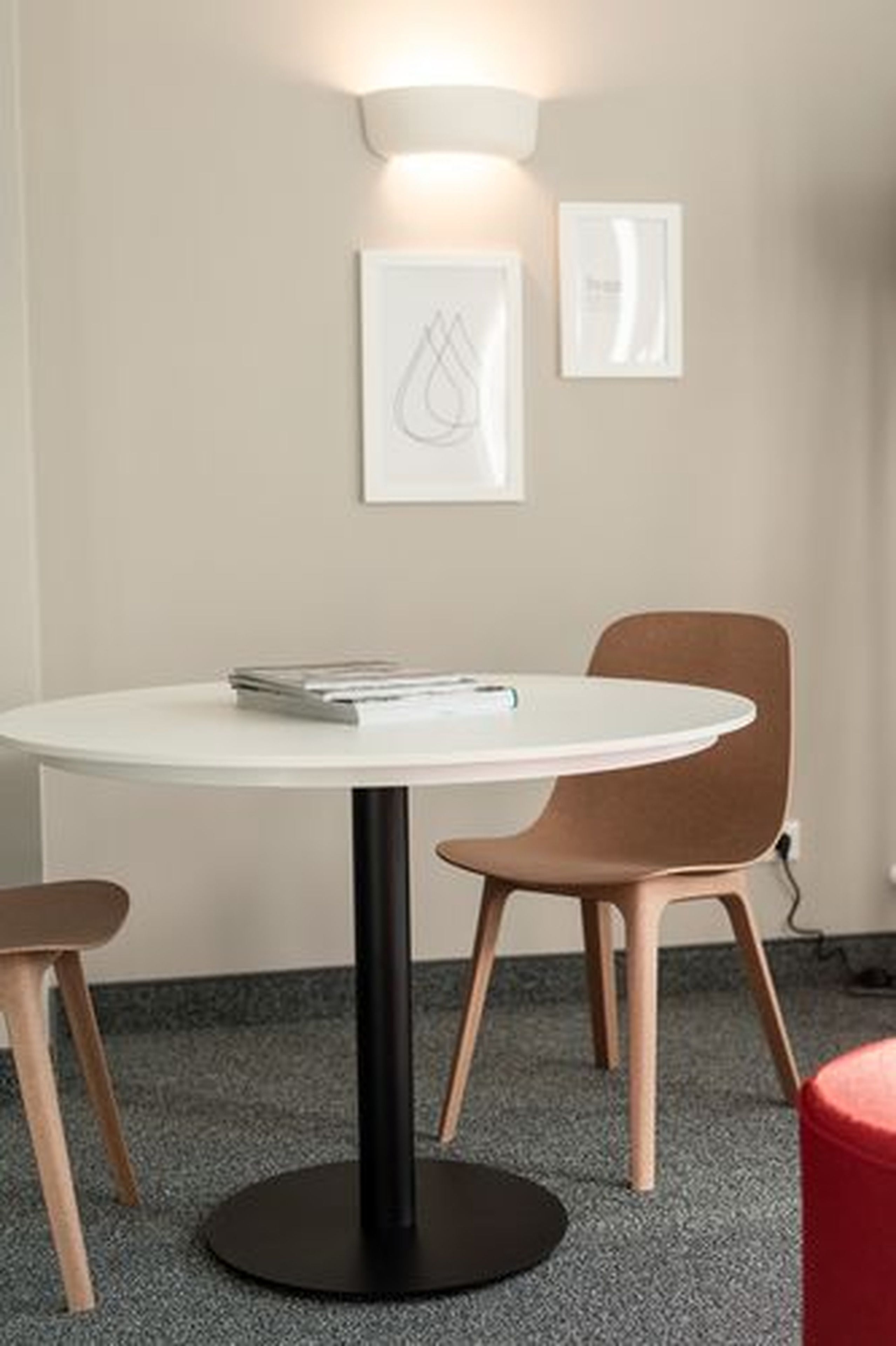 A round table with a black base, accompanied by two brown chairs and a red ottoman.