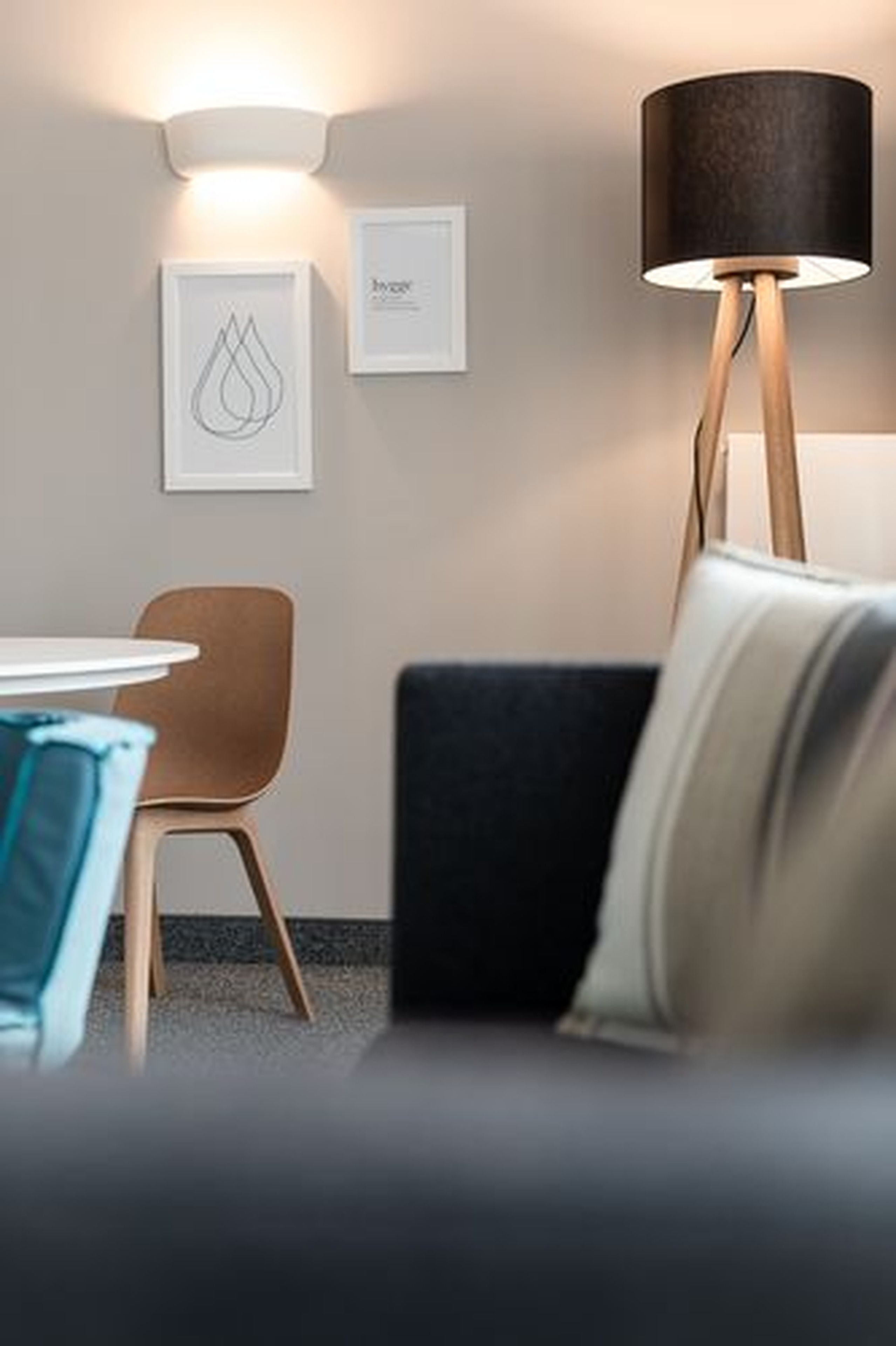 A modern room with a round table, a brown chair, a black sofa, a floor lamp, and two framed artworks on the wall.