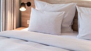 A hotel room with a bed, a nightstand, a lamp, and a curtain. - sylc. Apartmenthotel (Hamburg)