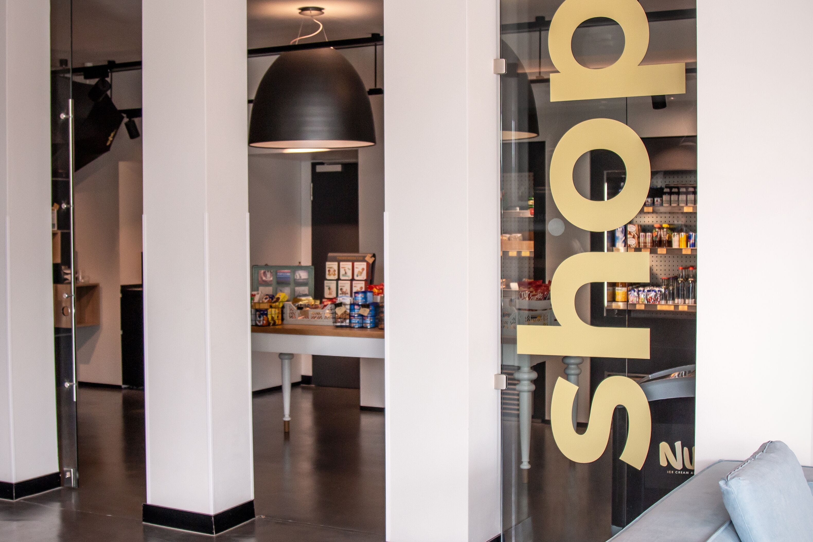 A modern interior with a large 'shop' sign, a counter with various products, and a hanging light fixture.