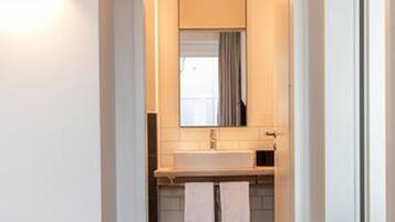 Una habitación de hotel con cama, un banco de madera, una mesita, un lavabo y un espejo.