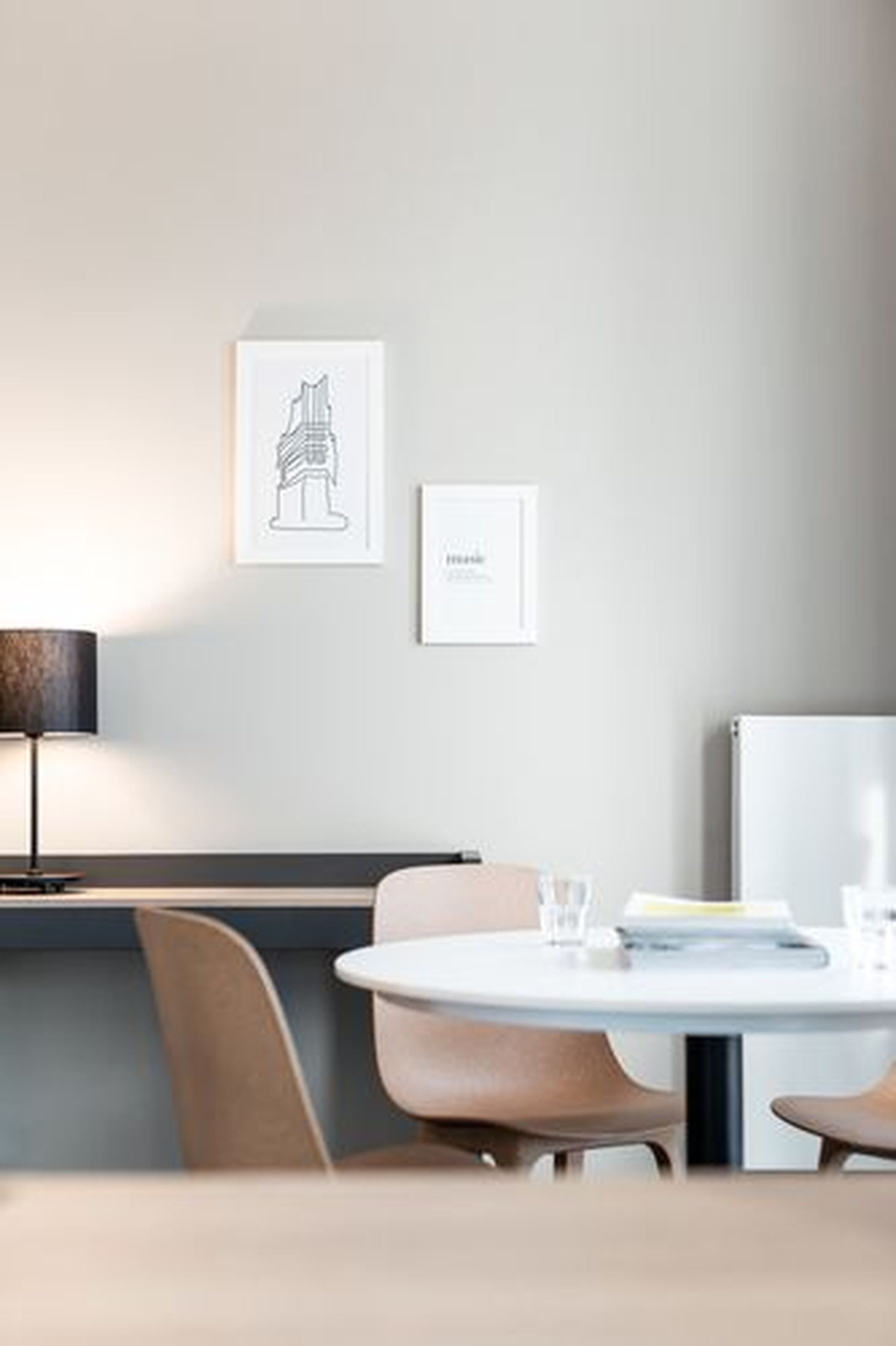 A modern room with a round table, two chairs, a lamp, and two framed artworks on the wall.