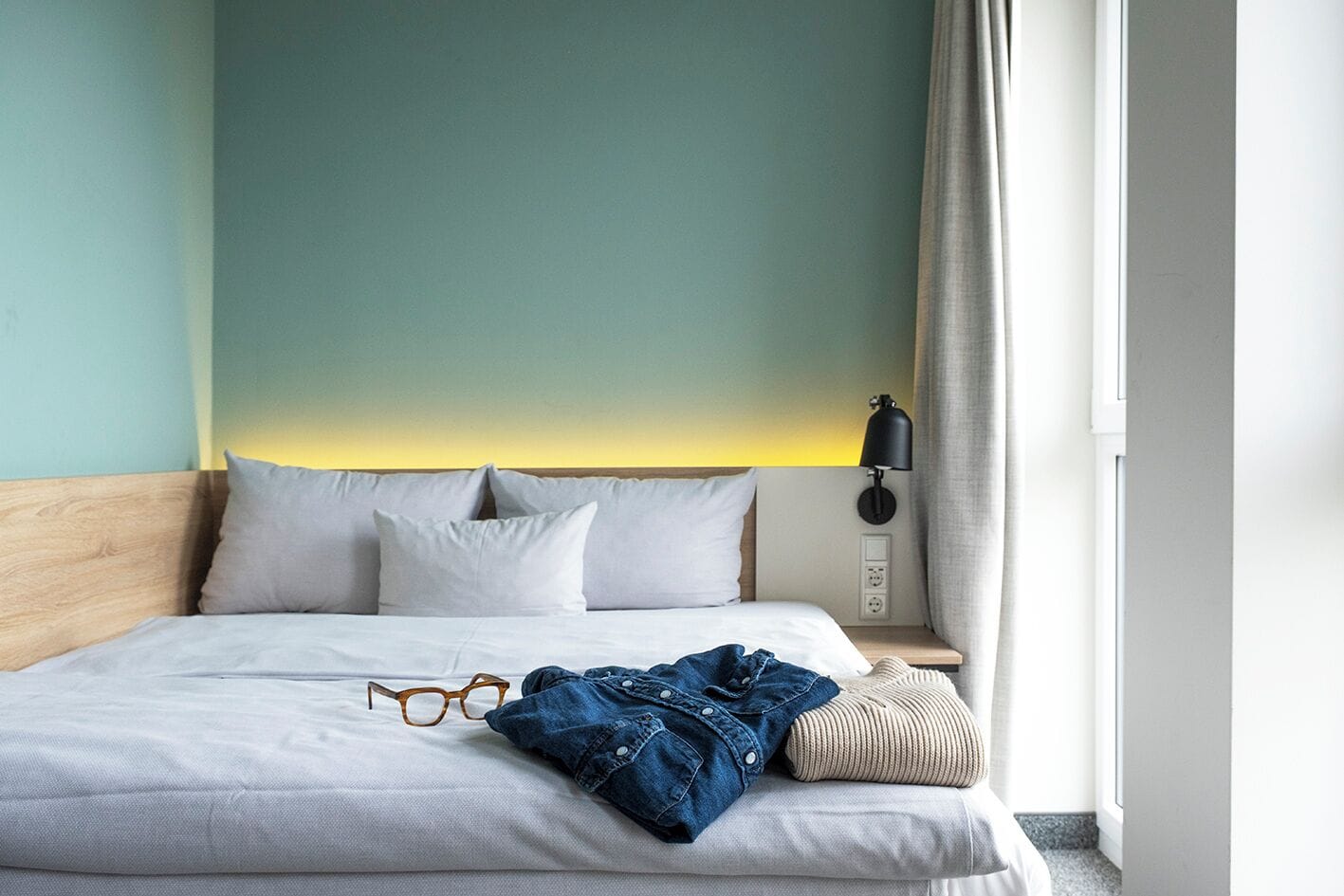 Un letto rifatto con lenzuola bianche, una testiera in legno e una lampada da comodino.