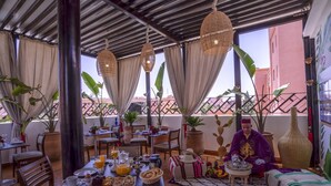 A dining area with tables set for breakfast, a person in traditional attire, and potted plants. - Majorelle City Center Boutique Hôtel (Marrakech)