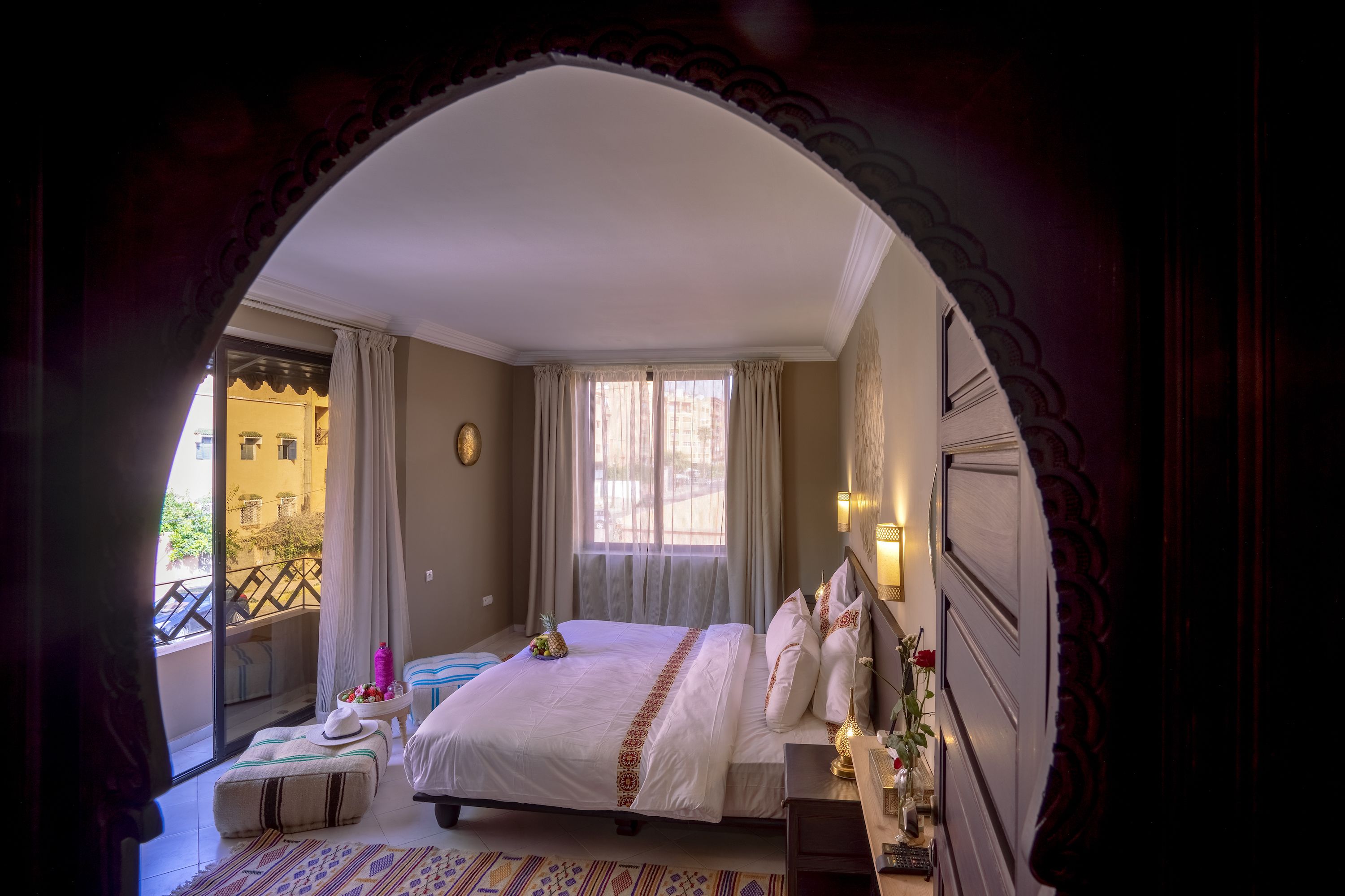 A hotel room with a large bed, a small table with a hat, a decorative wall, and a balcony with a railing.