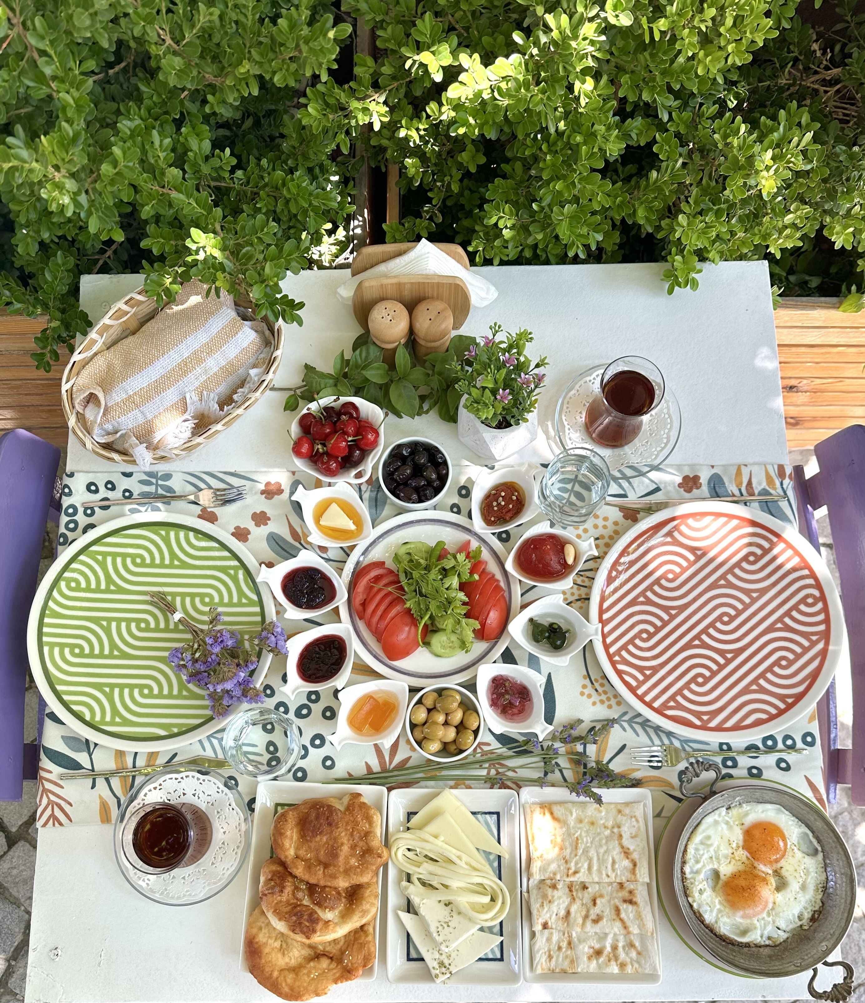 Une table dressée avec divers plats et boissons, entourée de verdure.