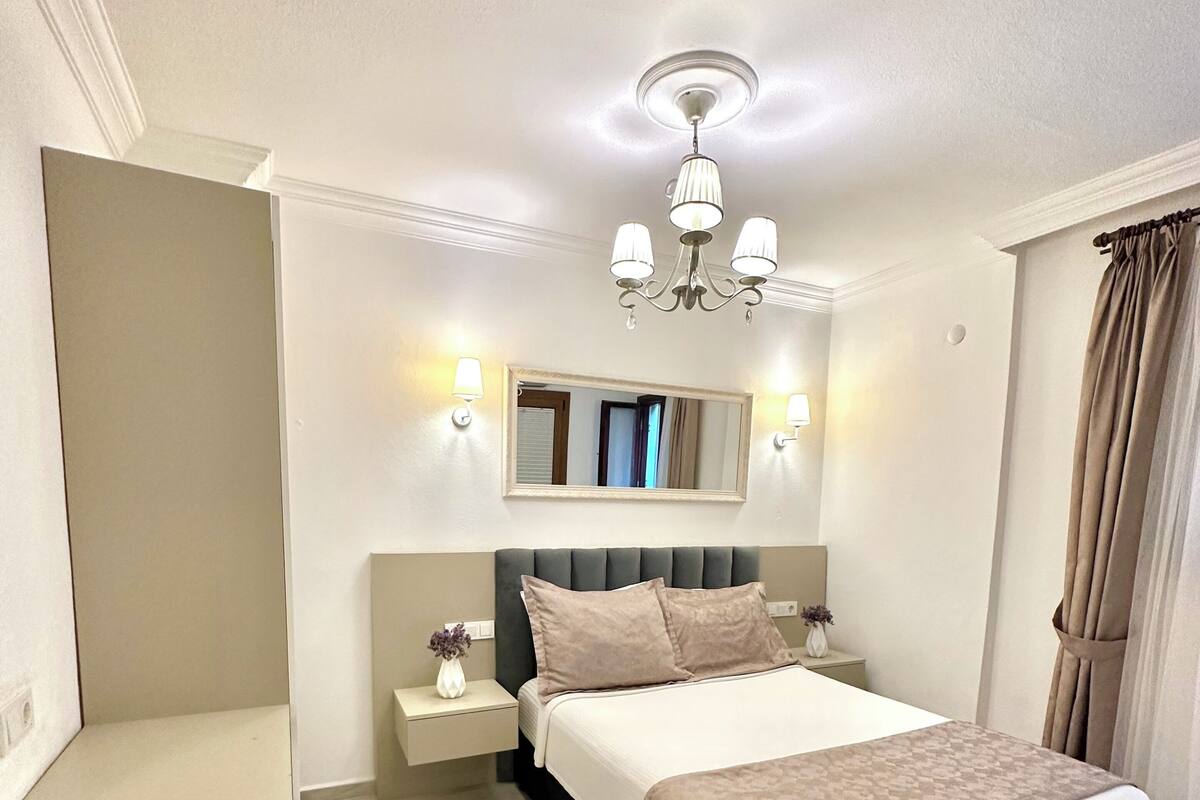 A bedroom with a bed, bedside tables, a mirror, a chandelier, and a window with curtains.
