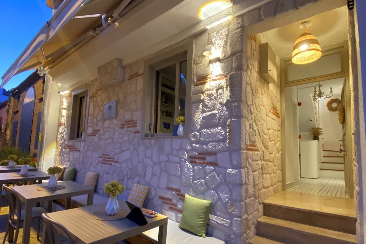 A stone building with outdoor seating, a staircase leading to the entrance, and a doormat with the name 'EVREN BOZCADA'.