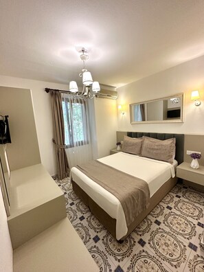A hotel room with a large bed, a bedside table with a lamp, a mirror, and a chandelier. - Evren Butik Otel (Bozcaada)