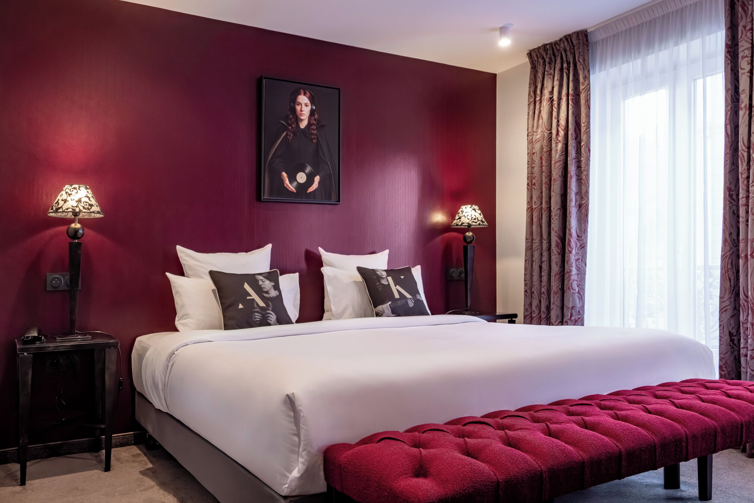A bedroom with a large bed, two bedside tables, a red bench, and a framed picture on the wall.