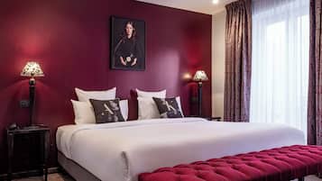 A bedroom with a large bed, two bedside tables, a red bench, and a framed picture on the wall.