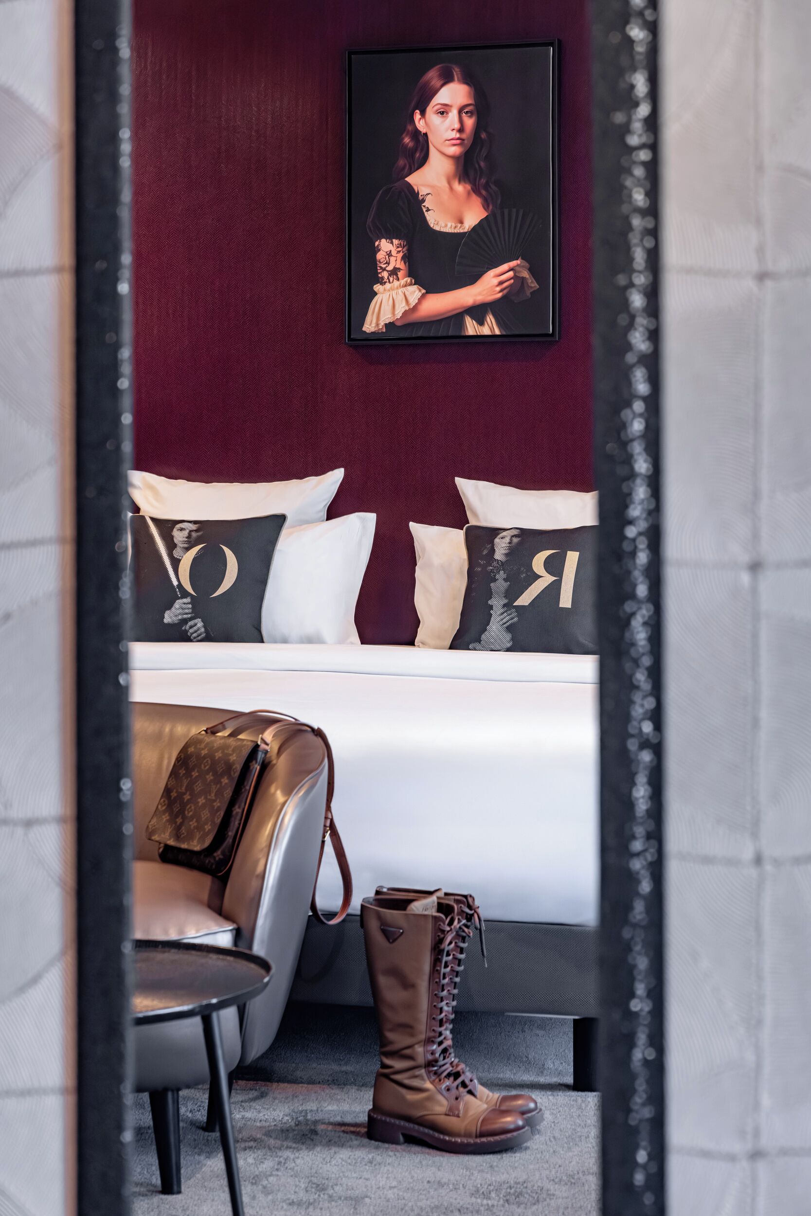 A bedroom with a bed, pillows, a framed picture, a chair, and a pair of boots.
