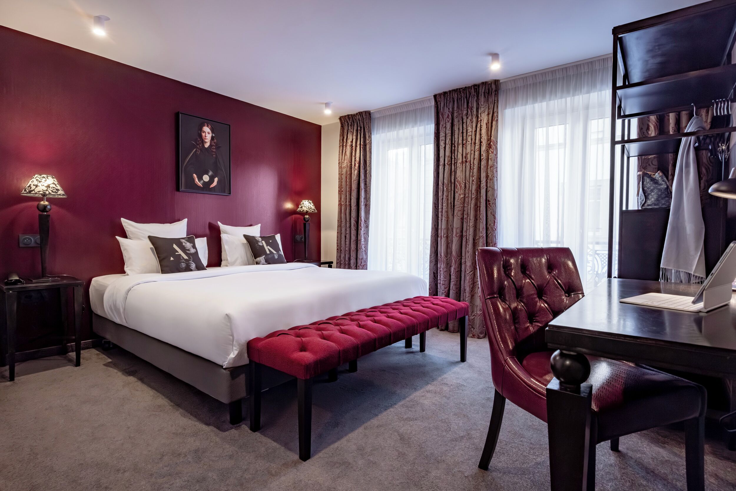A hotel room with a large bed, a red bench, a desk with a chair, and a wardrobe.