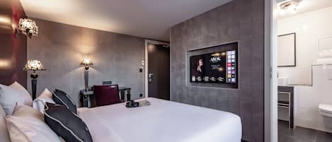 Una habitación de hotel moderna con una cama grande, lámparas de noche, un televisor montado y un baño a la vista.