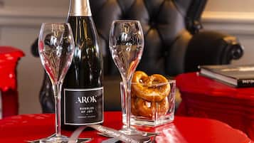Une table rouge sur laquelle se trouvent une bouteille de champagne Arok, deux verres et un bretzel posé sur un sous-verre rouge.