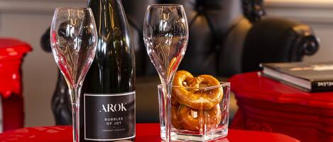 A red table with a bottle of Arok champagne, two glasses, and a pretzel on a red coaster.