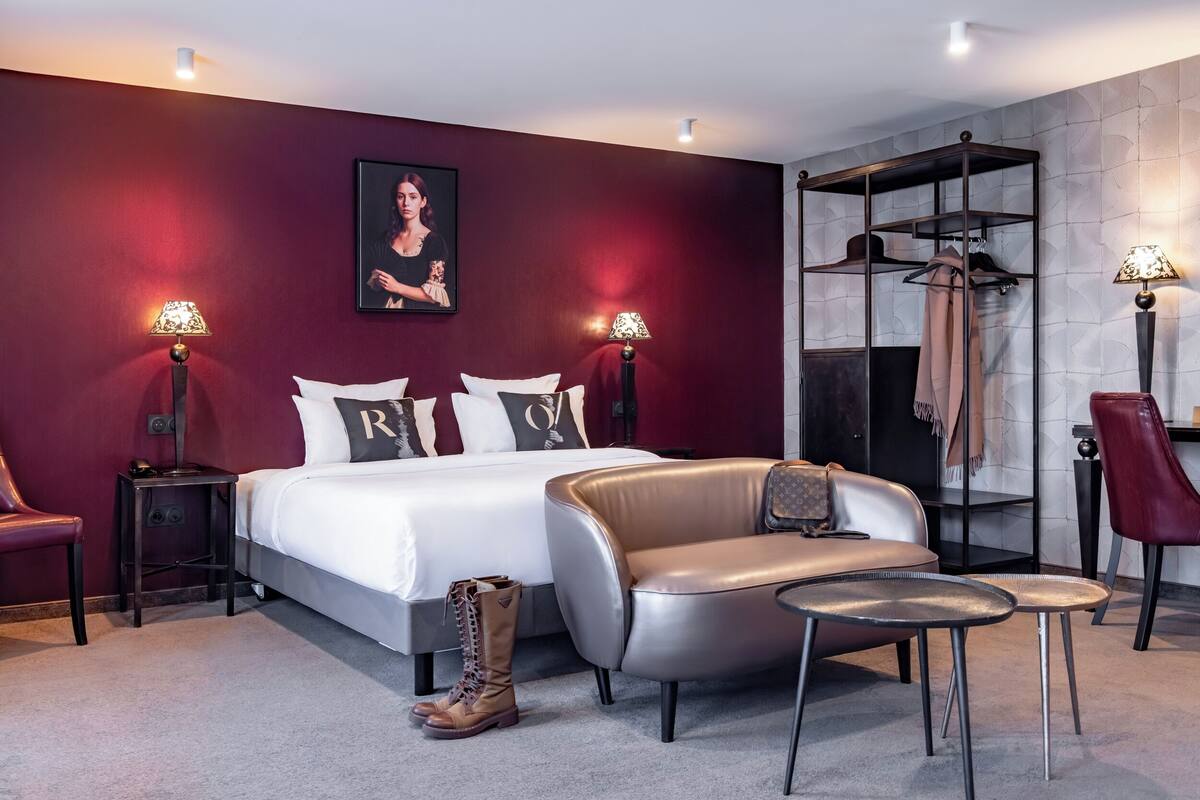 Moderni hotellihuone, jossa on suuri sänky, nahkasohva, kaksi pientä pöytää, punainen tuoli ja vaateteline.