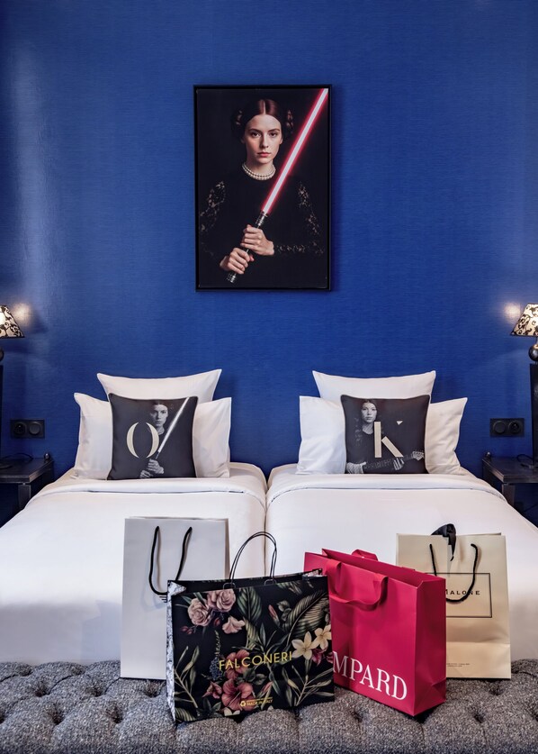 A hotel room with a blue wall, a framed artwork, two beds with matching pillows, and shopping bags on the floor. - Hotel Arok (Strasbourg)