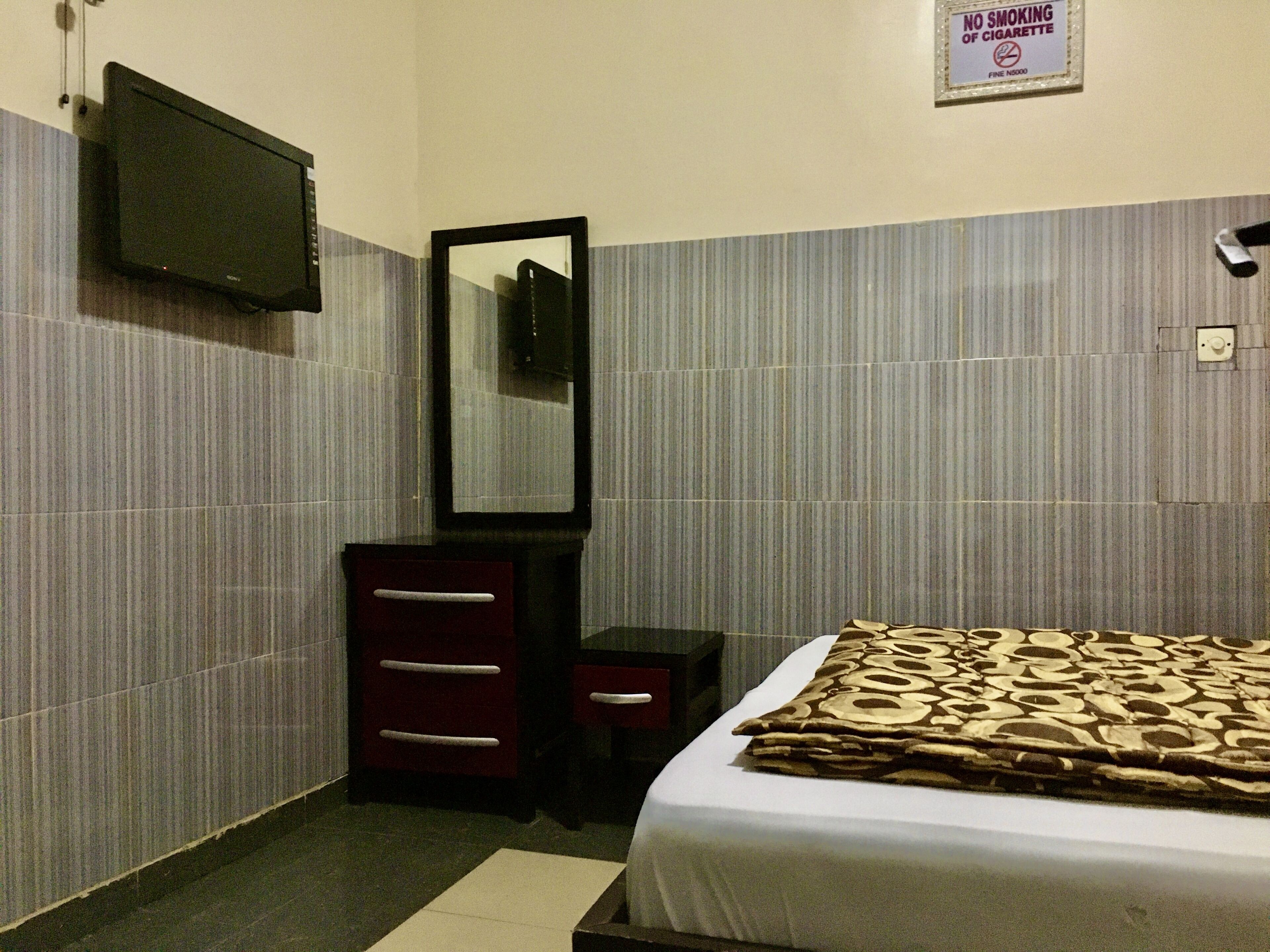 A hotel room with a bed, a dresser, a mirror, a television mounted on the wall, and a 'No Smoking' sign.