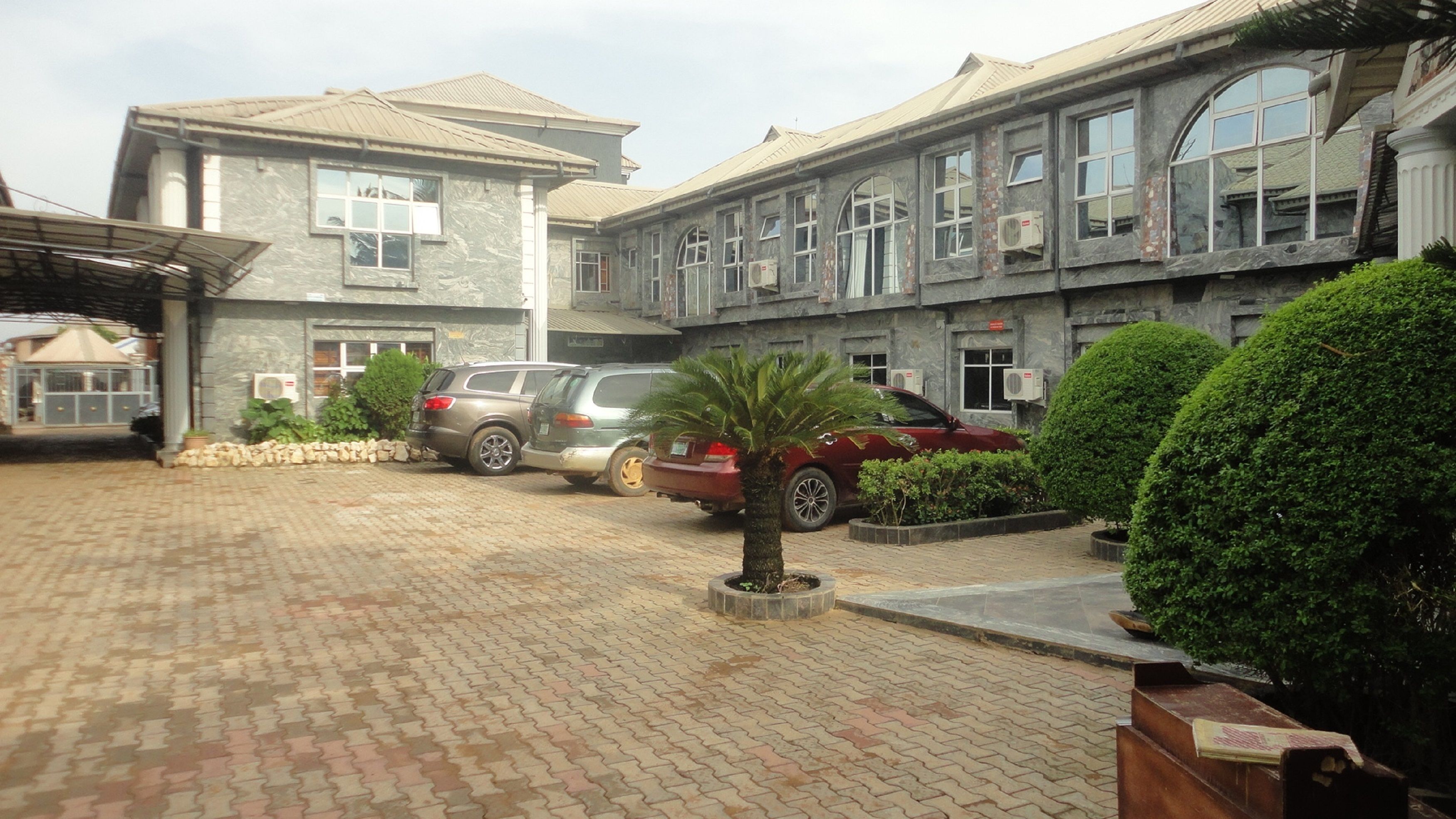 A building with a paved driveway, parked cars, and a palm tree.