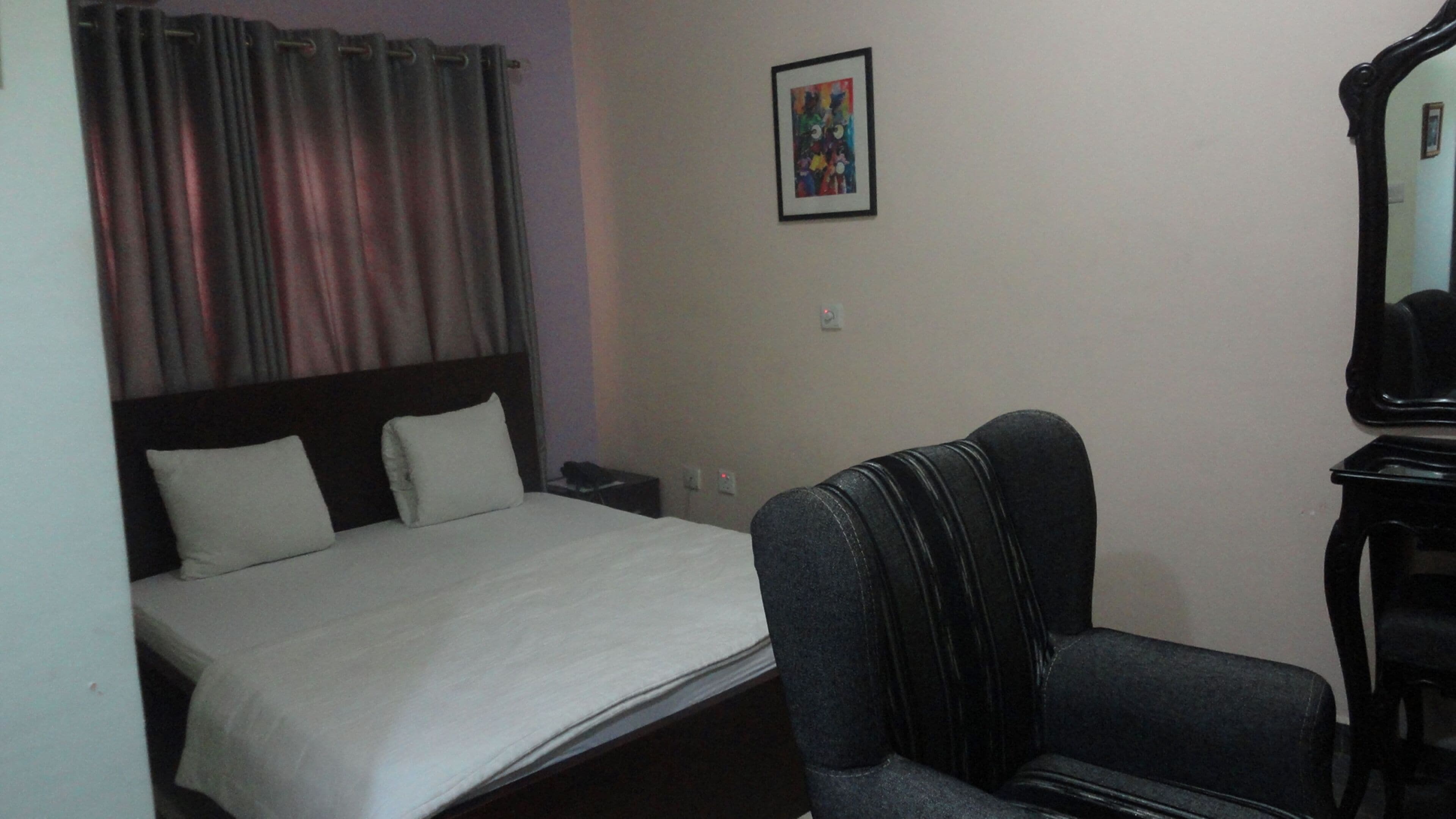 A hotel room with a bed, a chair, a desk, and a mirror.