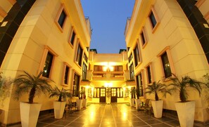 A hotel lobby with a central open space, potted plants, and a symmetrical architectural design. - Enkay Residency V Block-Cyber City (Gurugram)