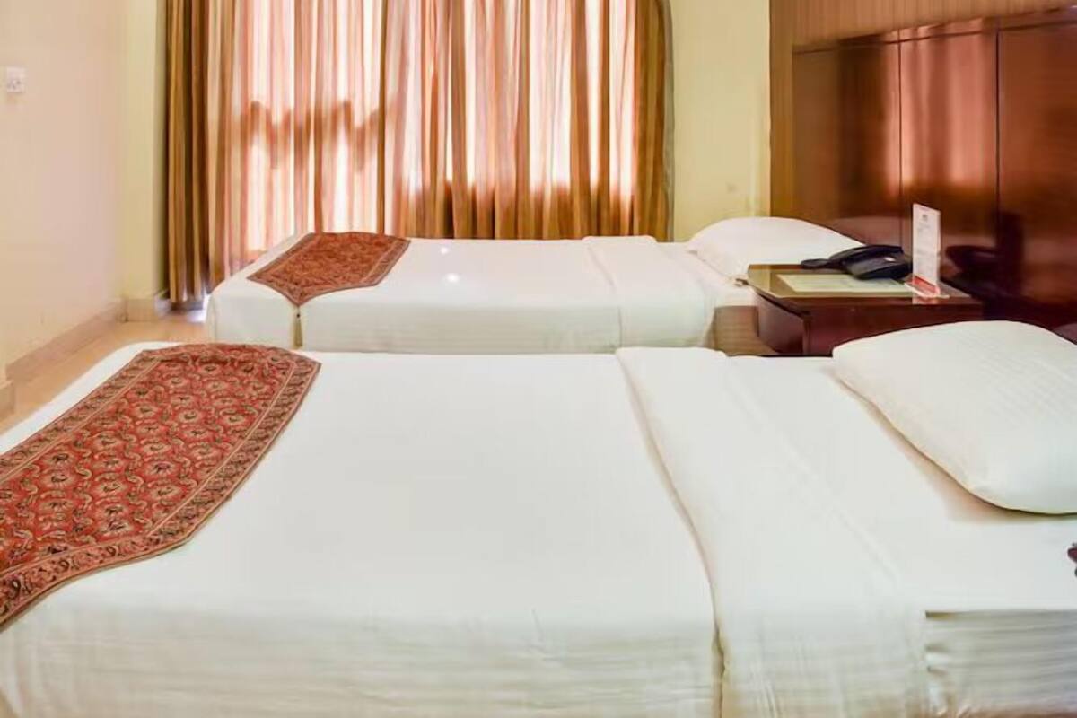 Ein Hotelzimmer mit zwei Betten, einem Holzschrank, einem Schreibtisch mit Telefon und einem roten Teppich mit Muster.