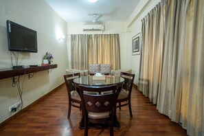 A dining area with a round table, chairs, a flat-screen TV, and an air conditioning unit.