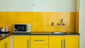 A kitchen with yellow cabinets, a microwave, a sink, and a power outlet on the wall. - Enkay Residency V Block-Cyber City (Gurugram)