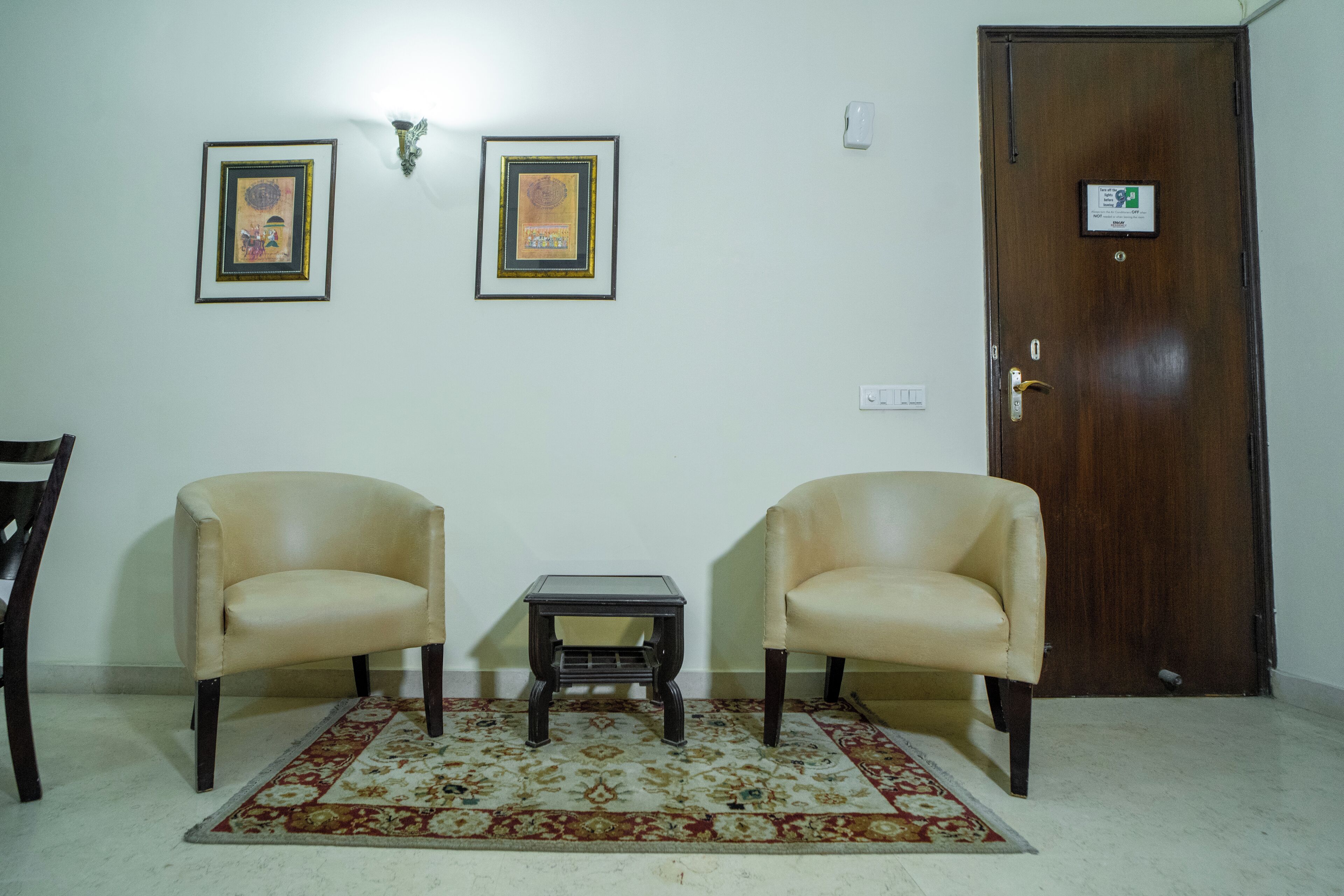 Um quarto com duas poltronas de couro, uma mesinha, um tapete estampado e uma porta de madeira.