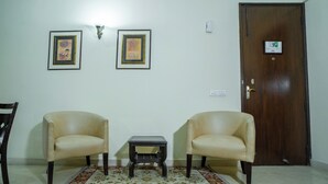 A room with two leather armchairs, a small table, a patterned rug, and a wooden door. - Enkay Residency V Block-Cyber City (Gurugram)