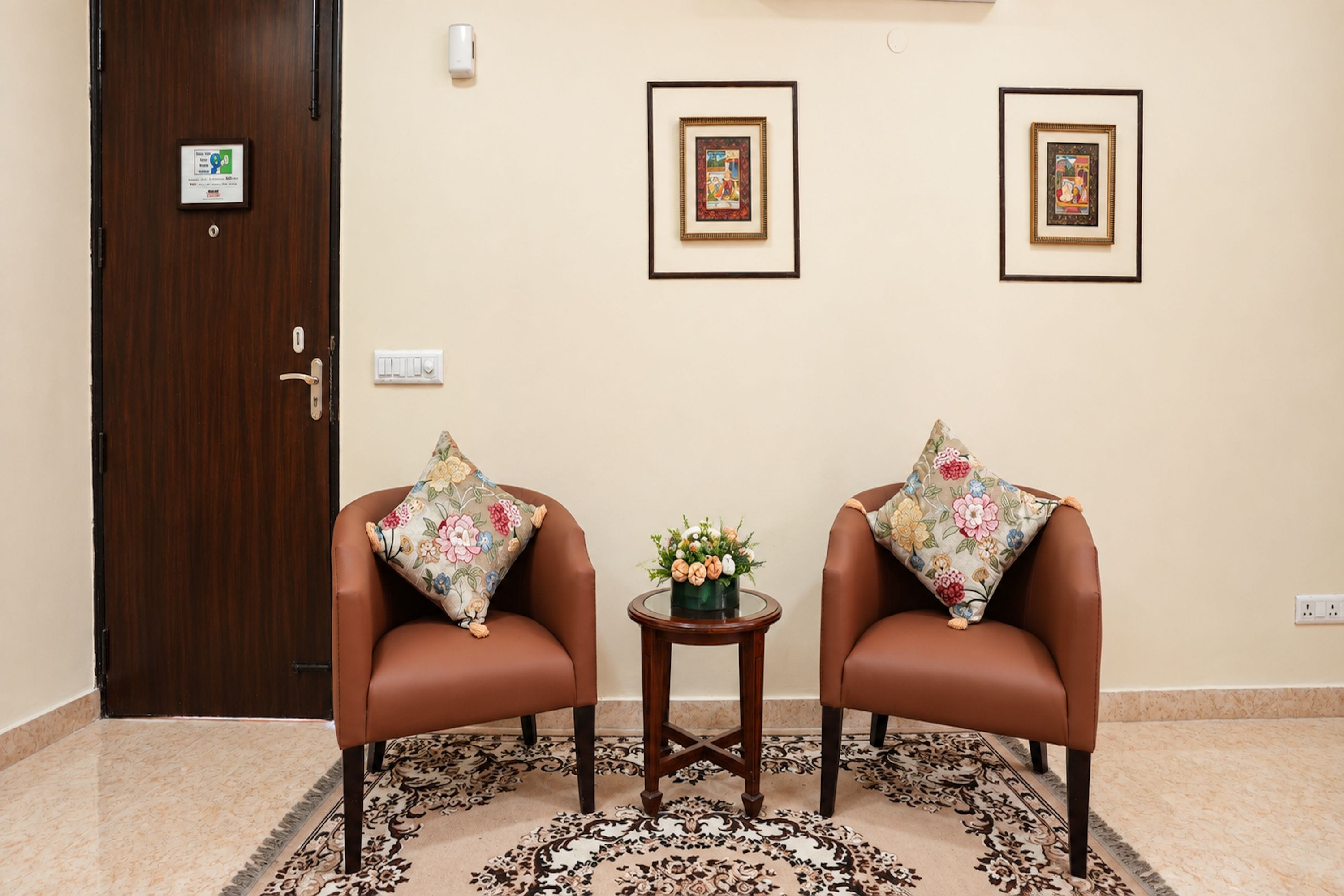 A room with two brown leather chairs, a small round table with a floral centerpiece, and a patterned rug on the floor.