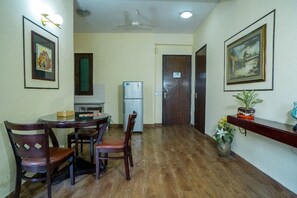 A dining area with a round table and chairs, a refrigerator, and framed artwork on the walls.