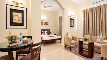 A hotel room with a bed, a sitting area with a sofa and chairs, a dining table with chairs, and a small table with a vase of flowers.