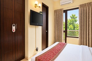 Habitación de hotel con cama, televisor en la pared, armario y ventana con cortinas.