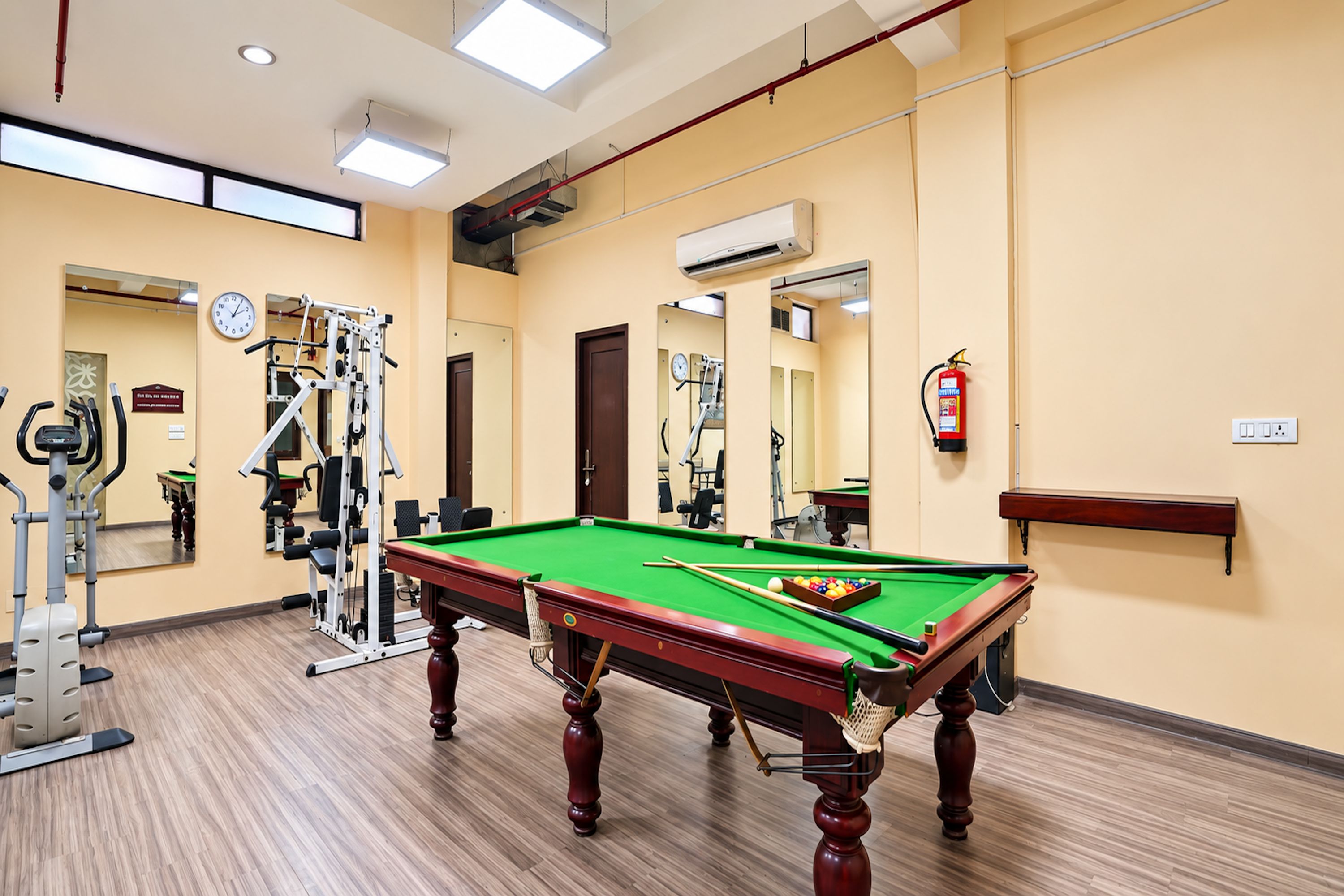 A billiards table in a room with exercise equipment and a fire extinguisher.