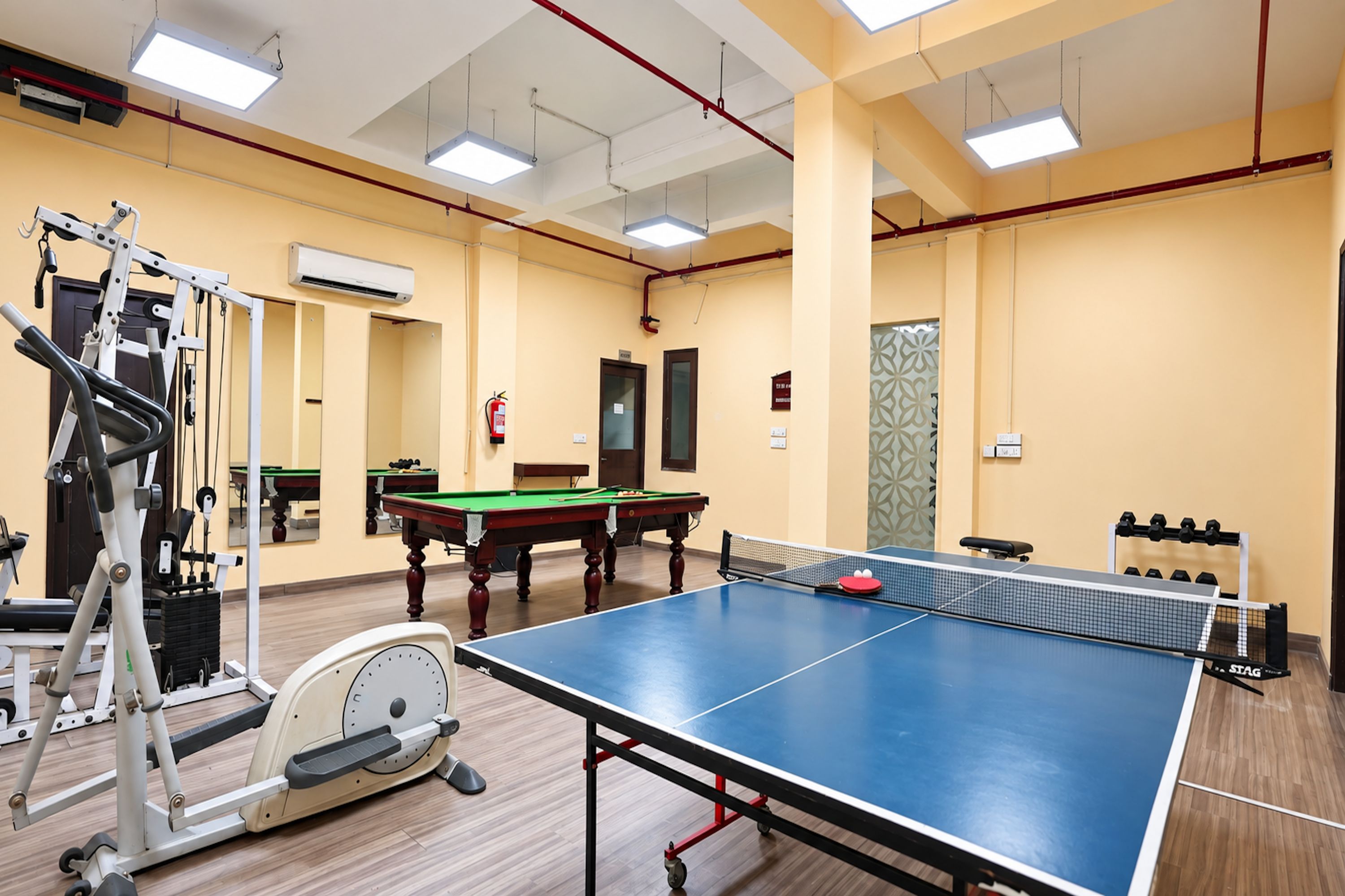 Une pièce équipée d’une table de ping-pong, de matériel d’exercice, d’une table de billard et d’une table de jeu de fléchettes.