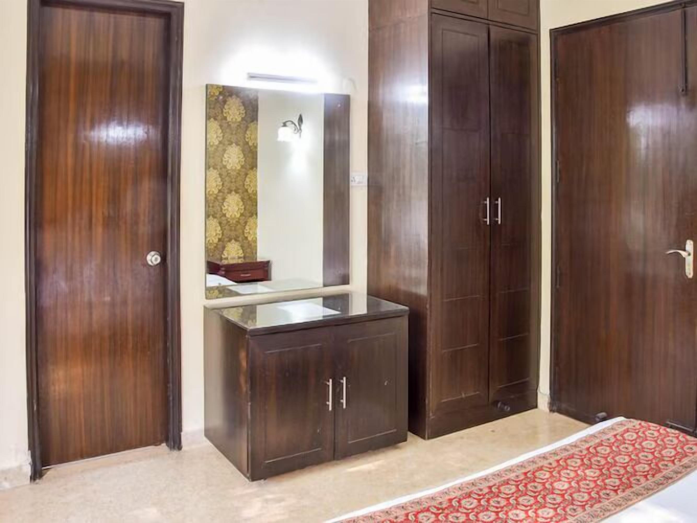 Quarto com guarda-roupa de madeira, espelho e tapete vermelho estampado.