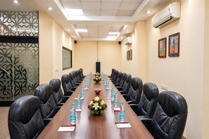 Une salle de conférence avec une longue table, des chaises en cuir noir, des bouteilles d’eau, des porte-noms et des compositions florales en guise de décoration centrale.